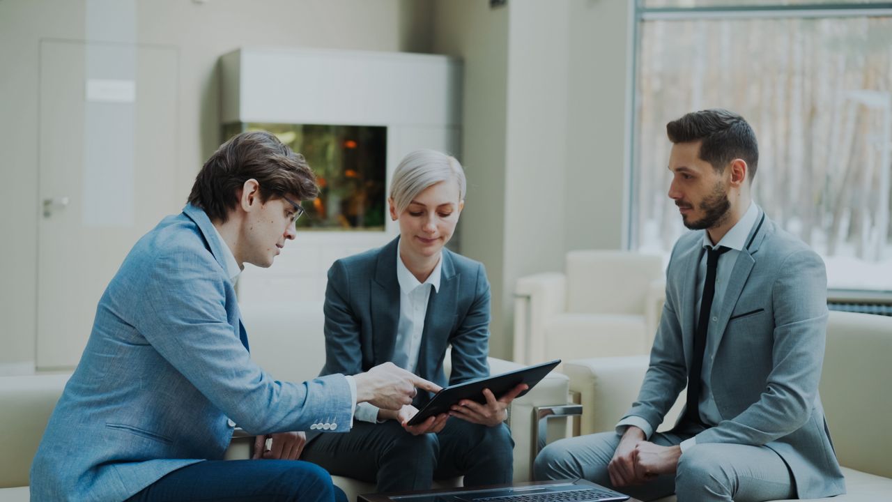services-02 Three professionals engaging in a business meeting in a modern office setting.