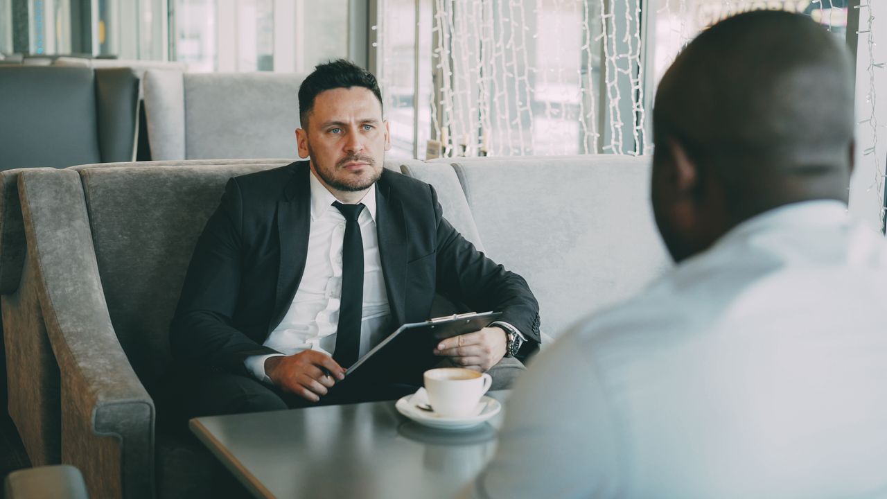 gallery-1 Two businessmen having a serious conversation over coffee in a stylish cafe setting.
